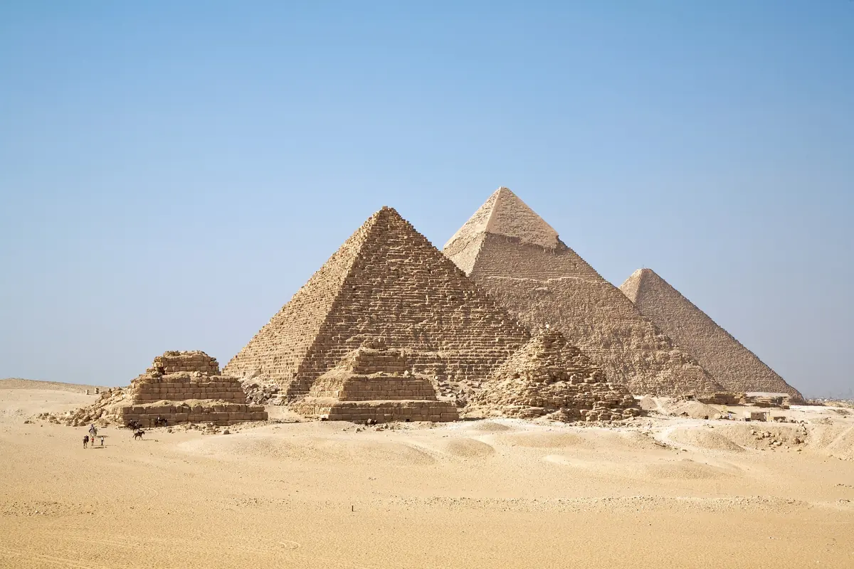 Die drei Pyramiden von Gizeh heute von Süden aus der Wüste: vorn die drei Königinnenpyramiden, dahinter die Mykerinos-Pyramide, die Chephren-Pyramide mit der hellen Kappe und rechts die Cheops-Pyramide, am rechten Rand die Stadt (Foto)