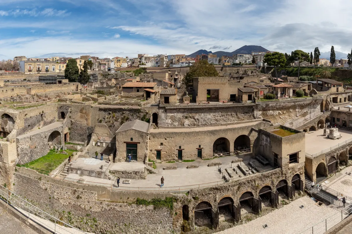 Die Ausgrabung von Herculaneum heute von der Zugangsrampe: die Bogenreihe der Bootshäuser, die Terrasse des Balbus, die Häuser der Stadt, darüber Ercolano und der Vesuv (Foto)