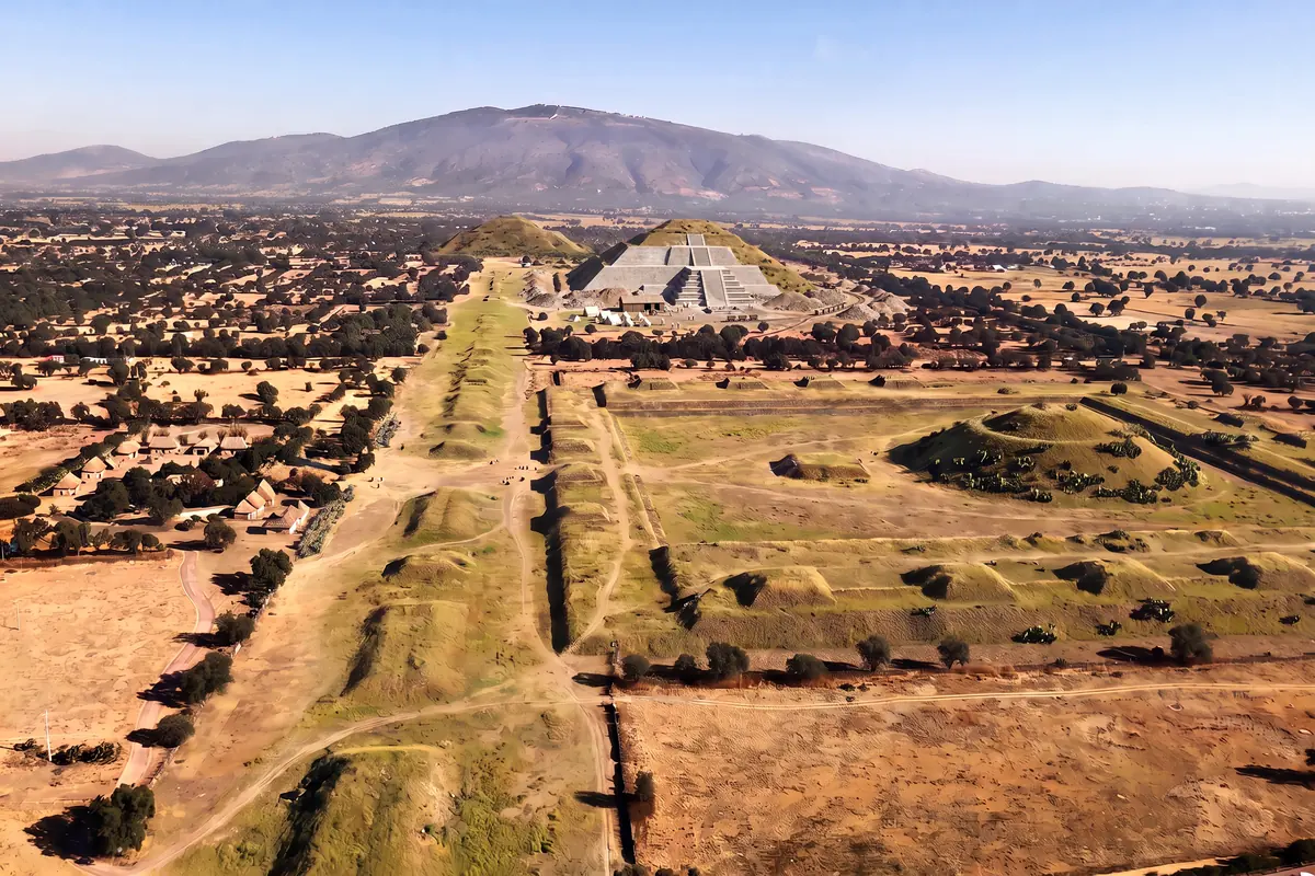 KI-Vision: die Ausgrabung der Sonnenpyramide um 1908 aus der Luft, eine Seite mit freigelegten Steinstufen, Schutthalden, Feldbahngleise mit Loren, Zelte, die Straße der Toten und die Ciudadela noch als überwachsene Hügel