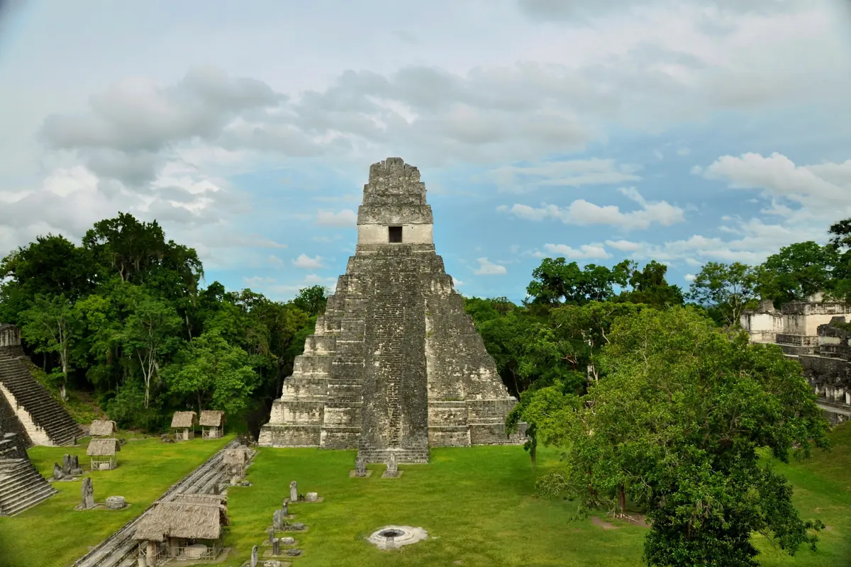 Die Große Plaza von Tikal heute, Blick von Tempel II auf Tempel I, links die Stelen unter Strohdächern vor der Nordakropolis, rechts die Zentralakropolis (Foto)